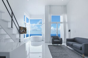 Un soggiorno moderno con una scala, una grande finestra vista mare, una vasca da bagno tonda, un divano grigio e una lampada da terra.