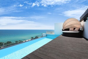 Un terrazzo in legno con piscina che si affaccia sul mare, un'area salotto coperta e un cielo sereno.
