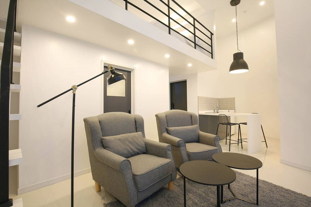 A modern living room with two grey armchairs, a black floor lamp, and a small white table.