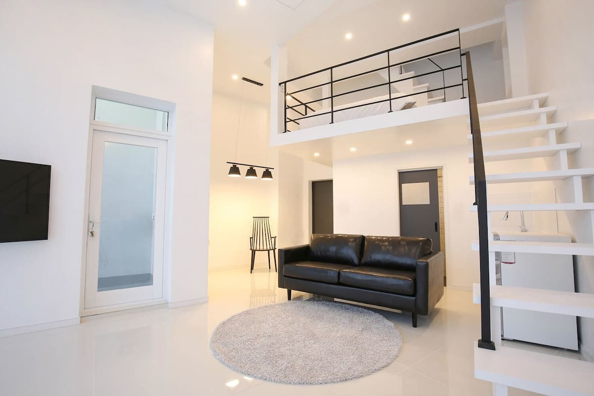 A modern living room with a black leather sofa, a round rug, a staircase, and a TV mounted on the wall.