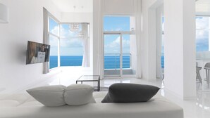 Una sala de estar moderna con un sofá blanco, una mesa de centro de vidrio y un amplio ventanal con vistas al océano.