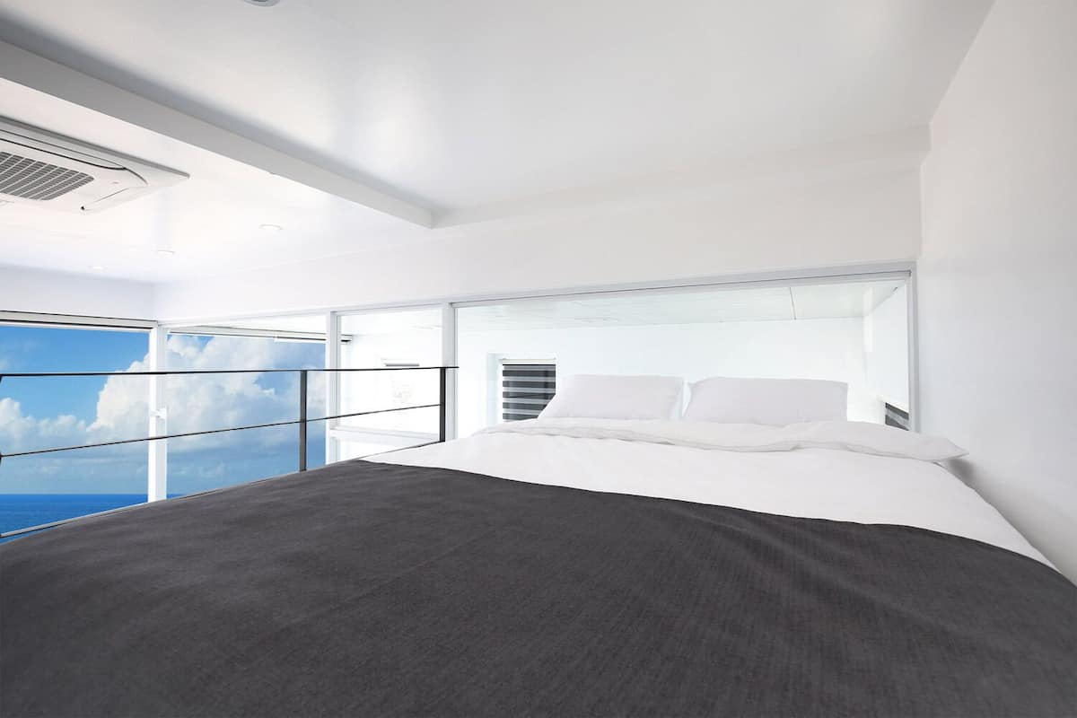 A modern bedroom with a large bed, a view of the ocean through a balcony, and a skylight.