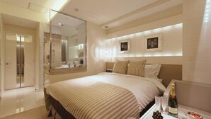 A hotel room with a large bed, a bedside table with a bottle of champagne, a mirror, and a wardrobe. - Hotel Glanz Cascata (Tokyo)