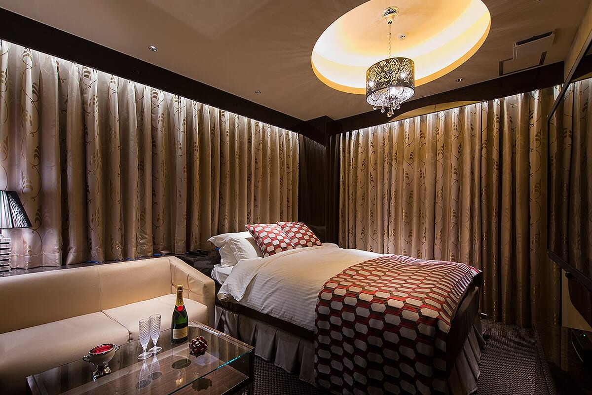 A hotel room with a large bed, a sofa, a glass coffee table, and a chandelier.