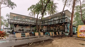 A modern building with a glass facade, outdoor seating area, and palm trees. - Roxy Sematan Villa & Townhouse (Lundu)