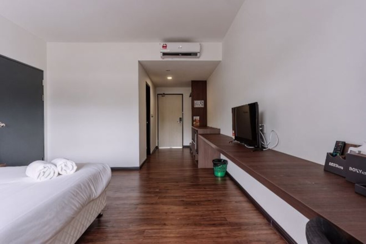 A hotel room with a bed, a desk, a television, and a small kitchenette area.
