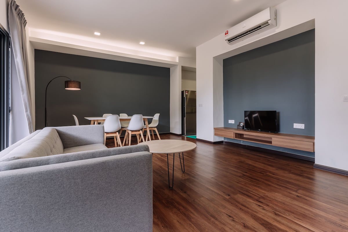A modern living room with a grey sofa, a round wooden table, and white chairs.