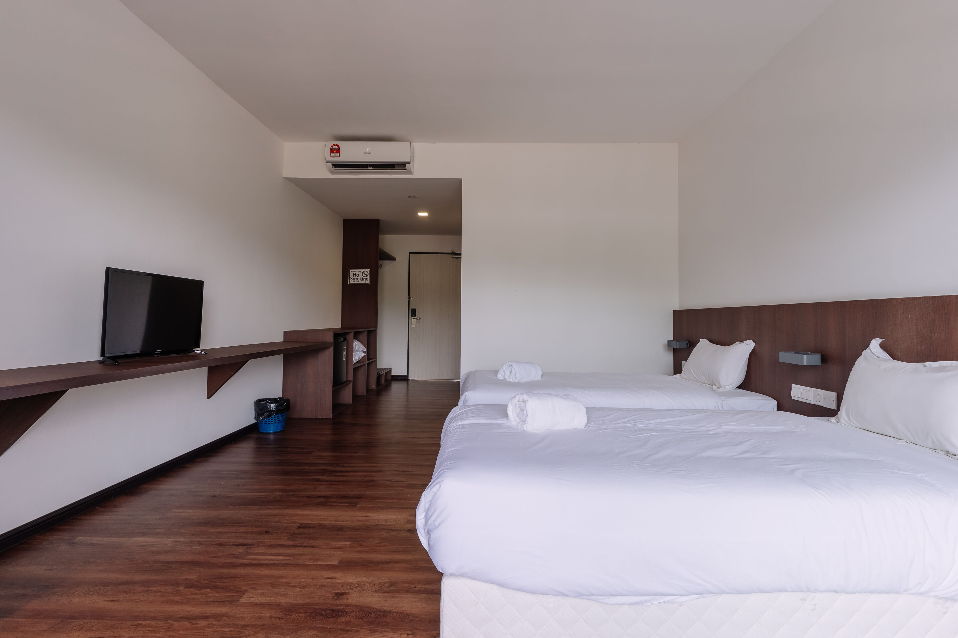 A hotel room with three beds, a TV, a desk, and a trash bin.