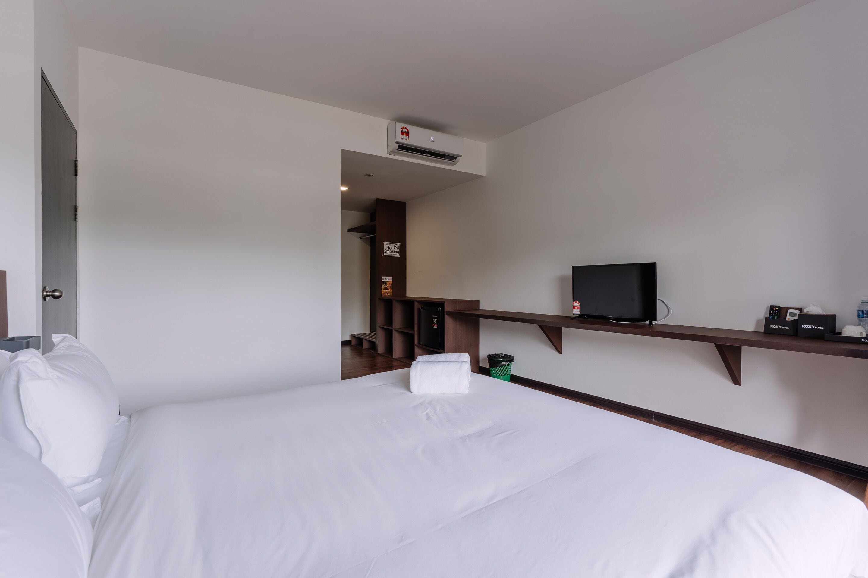 A hotel room with a bed, a television, a shelf with toiletries, and a door leading to another room.