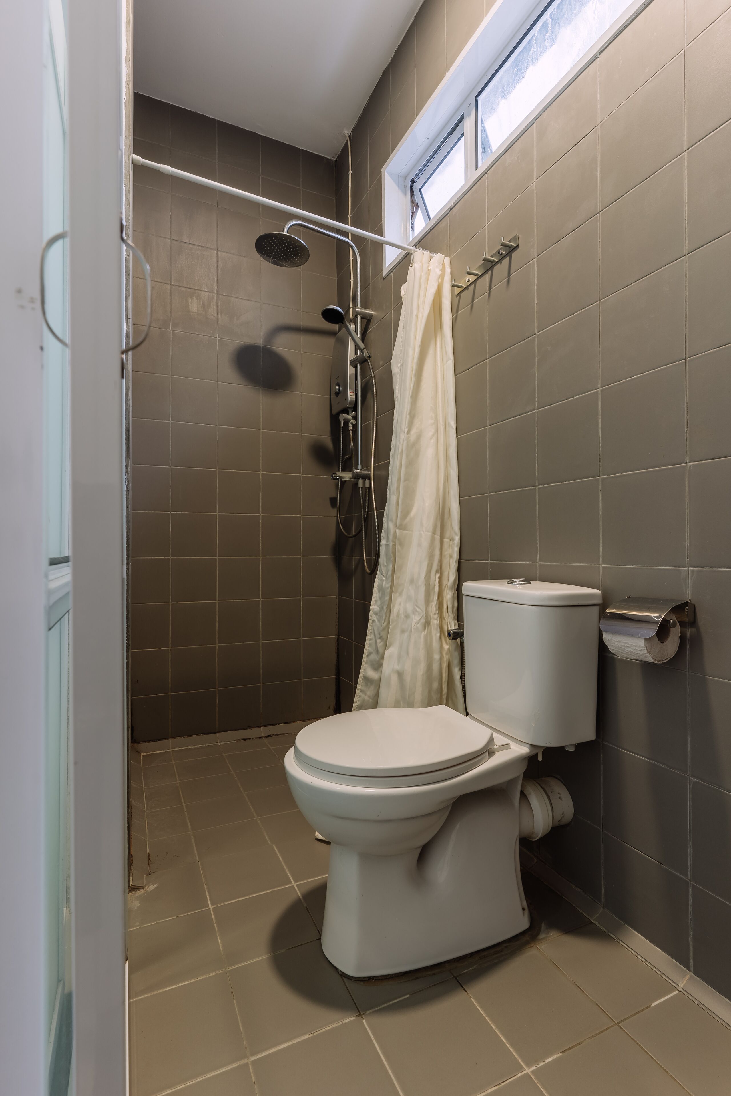 A bathroom with a toilet, shower, and a window.