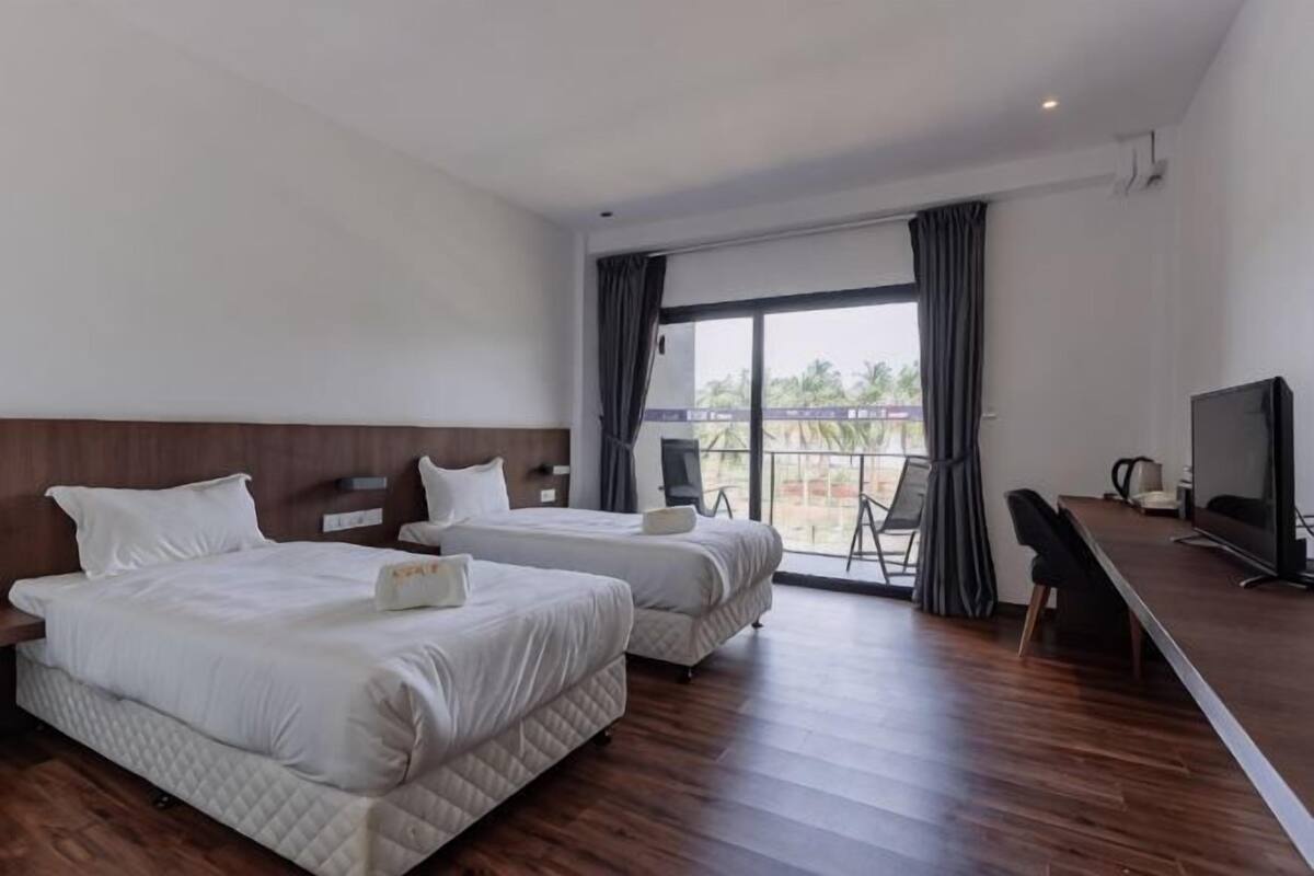 A hotel room with two beds, a TV, a desk, and a balcony with a view.