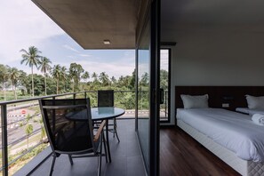 A balcony with a glass door leading to a bedroom with a bed and a table with chairs.
