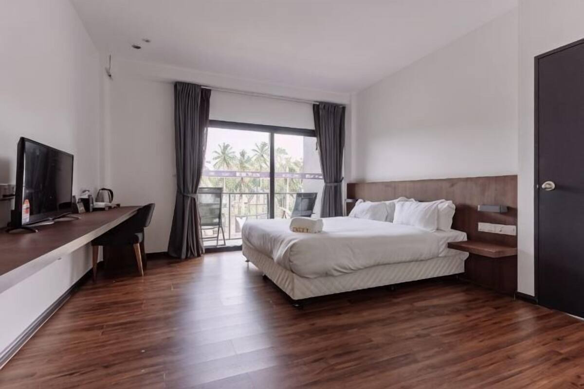 A hotel room with a bed, a desk, a TV, and a balcony with curtains.