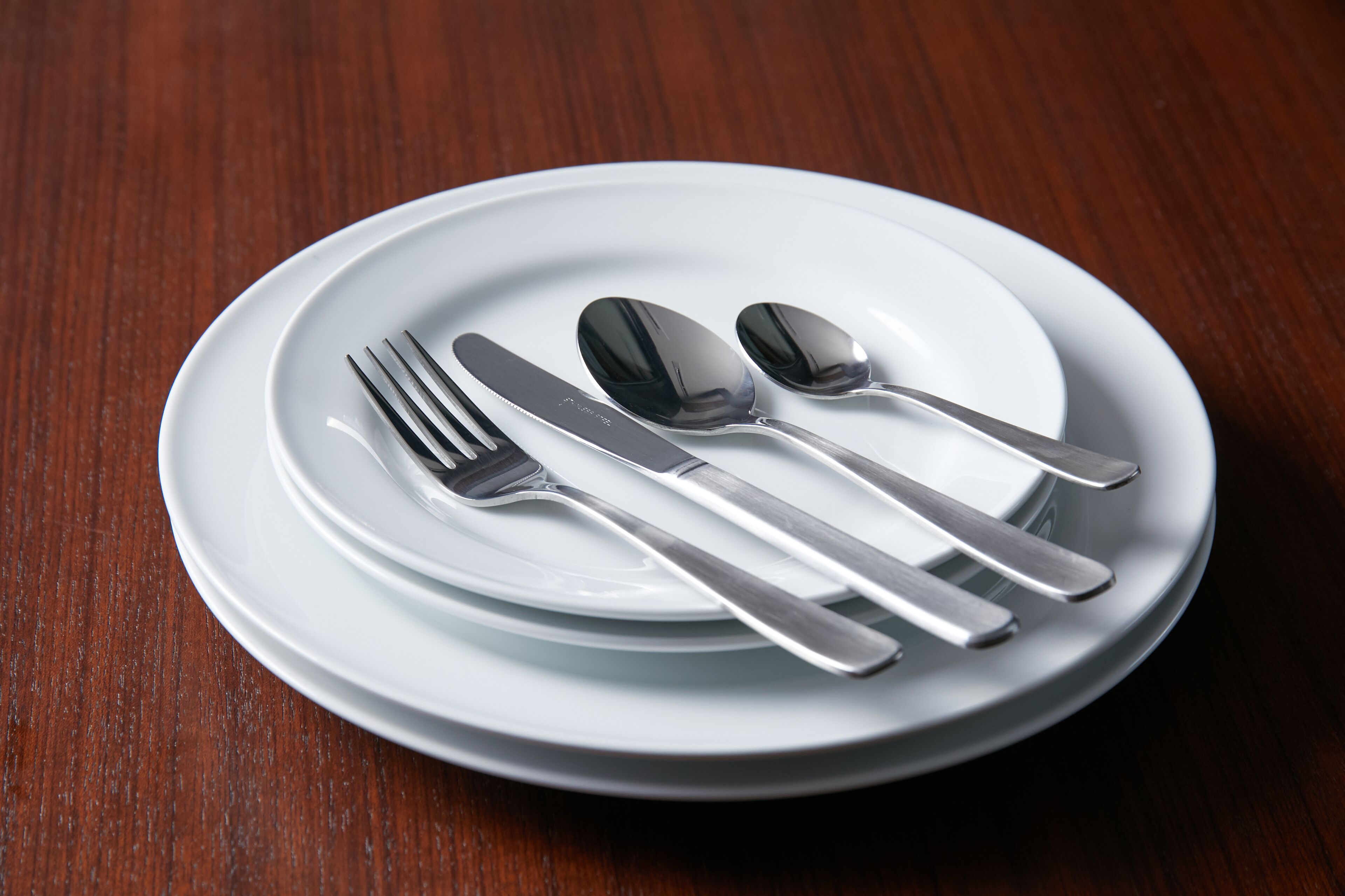 A white plate with a fork, knife, spoon, and a small bowl on a wooden table.