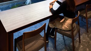 A woman sitting at a wooden table with a view of a building and a small indoor garden. - HOTEL KYOTOLOGY (Kyoto)