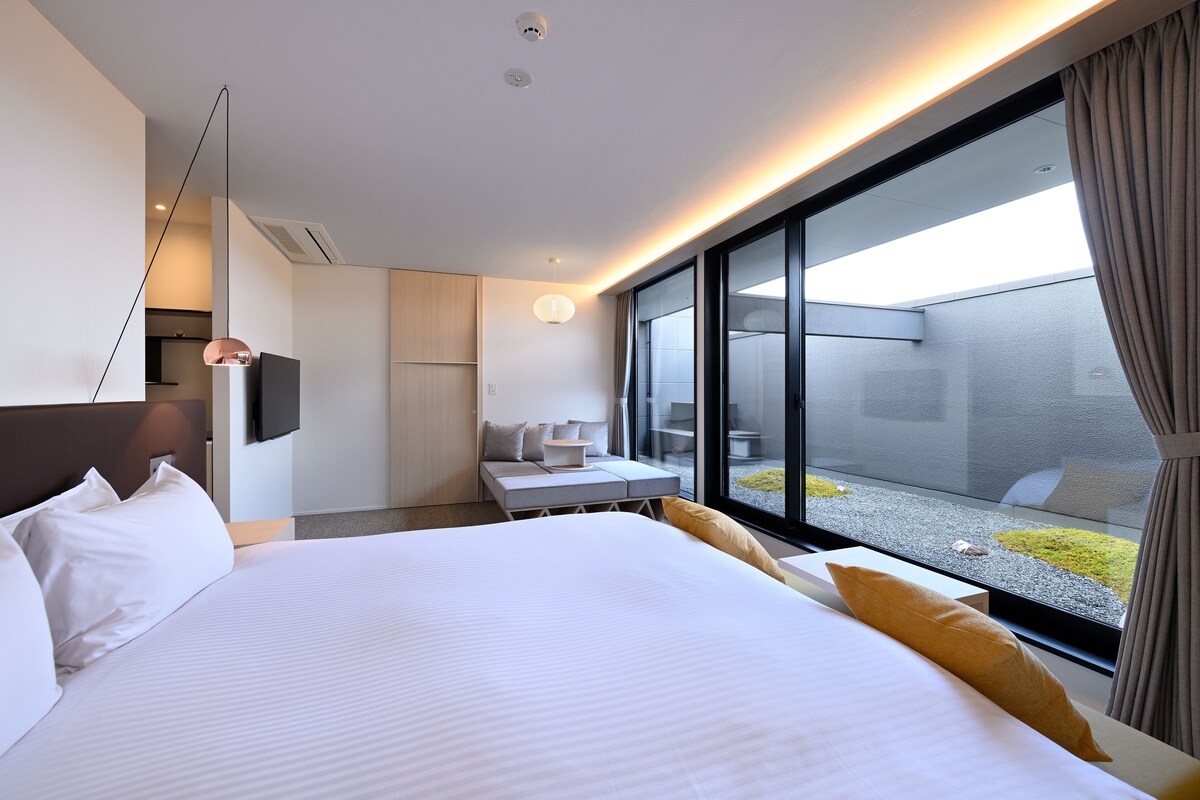 A modern hotel room with a large bed, a desk, and a view of a courtyard.