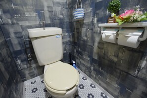 A bathroom with a toilet, a hanging blue and white striped bucket, a small potted plant, and a shelf with a sign reading "Sweet Home". - Balcone Uchikyuhoji (Osaka)