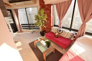 A modern living room with a glass coffee table, red sofa, and a large window with curtains.
