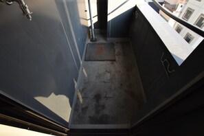 A narrow stairway with a metal handrail, a metal door at the top, and a concrete floor. - Balcone Uchikyuhoji (Osaka)