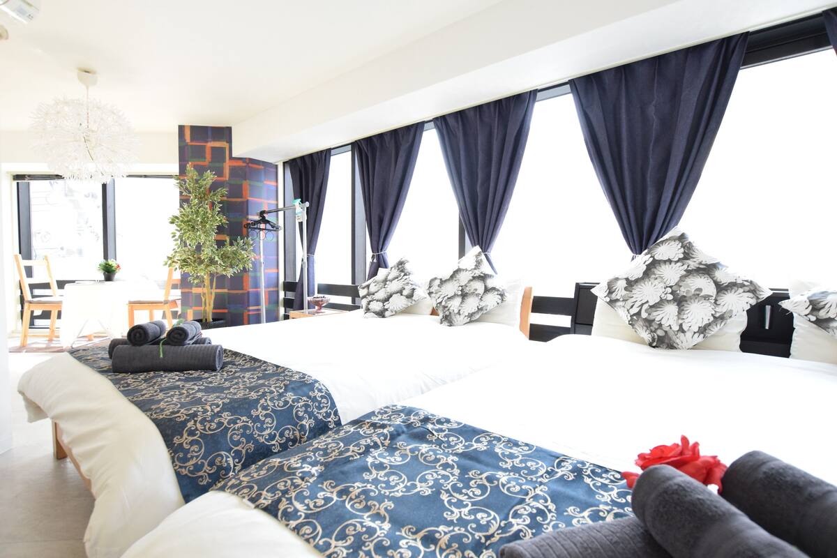 Quarto de hotel moderno com uma cama grande, cortinas escuras, um candelabro e vista para a cidade.
