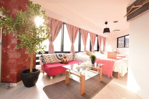 A modern living room with a glass coffee table, a red sofa, a potted plant, and a bed with pink curtains.