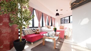 A modern living room with a red sofa, glass coffee table, and a large potted plant. - Balcone Uchikyuhoji (Osaka)