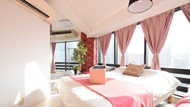 A modern bedroom with a large bed, a potted plant, and a city view through large windows. - Balcone Uchikyuhoji (Osaka)