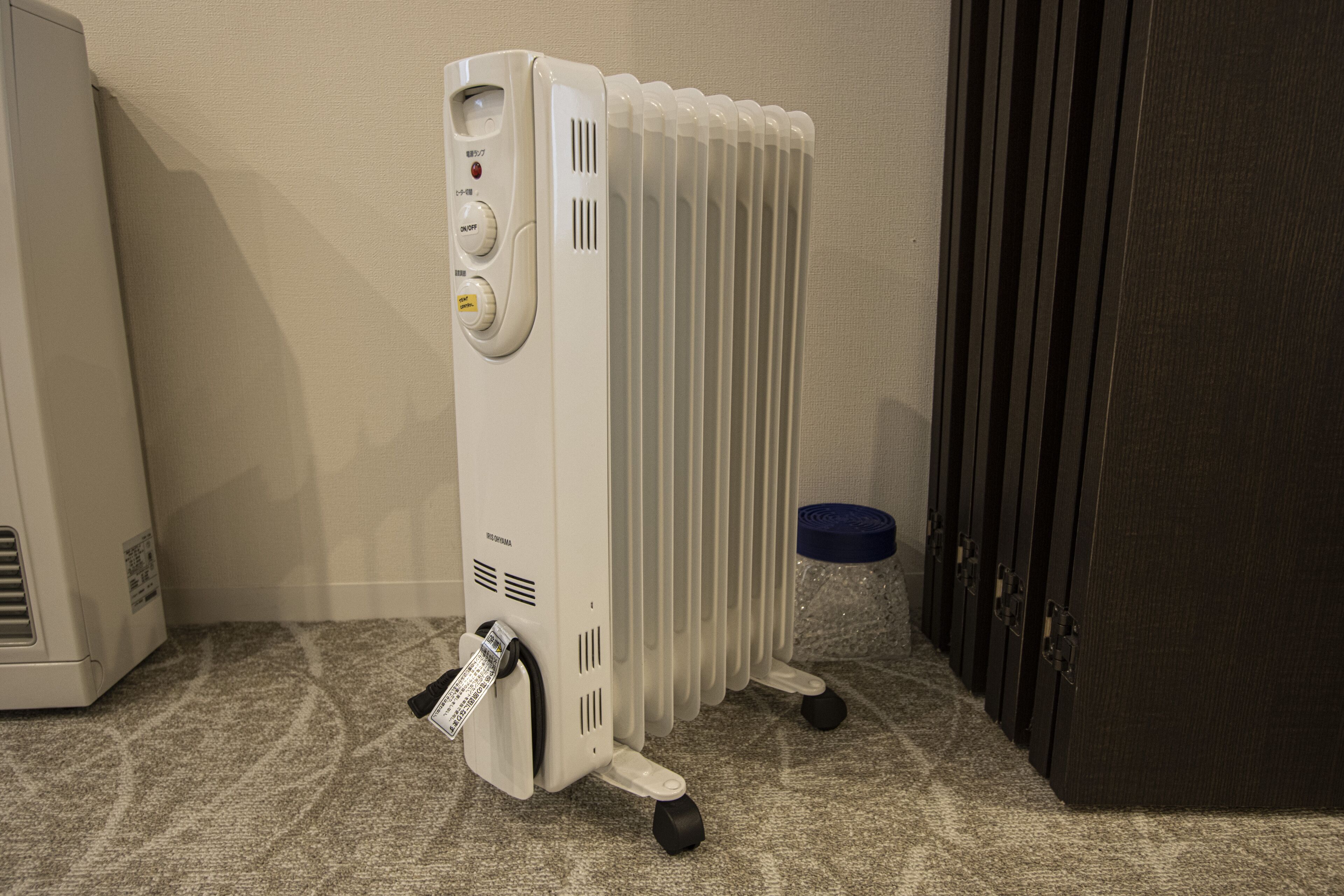 A portable heater with control buttons and a power cord, placed on a carpeted floor next to a door.