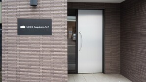A modern building entrance with a brick facade, a sign reading 'UCHI Susukino 5.7', and a door with a handle. - UCHI Susukino 5.7 (Sapporo)