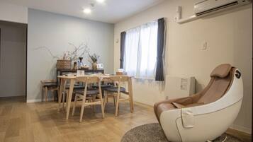 A modern living room with a dining area, a massage chair, and a window with curtains.