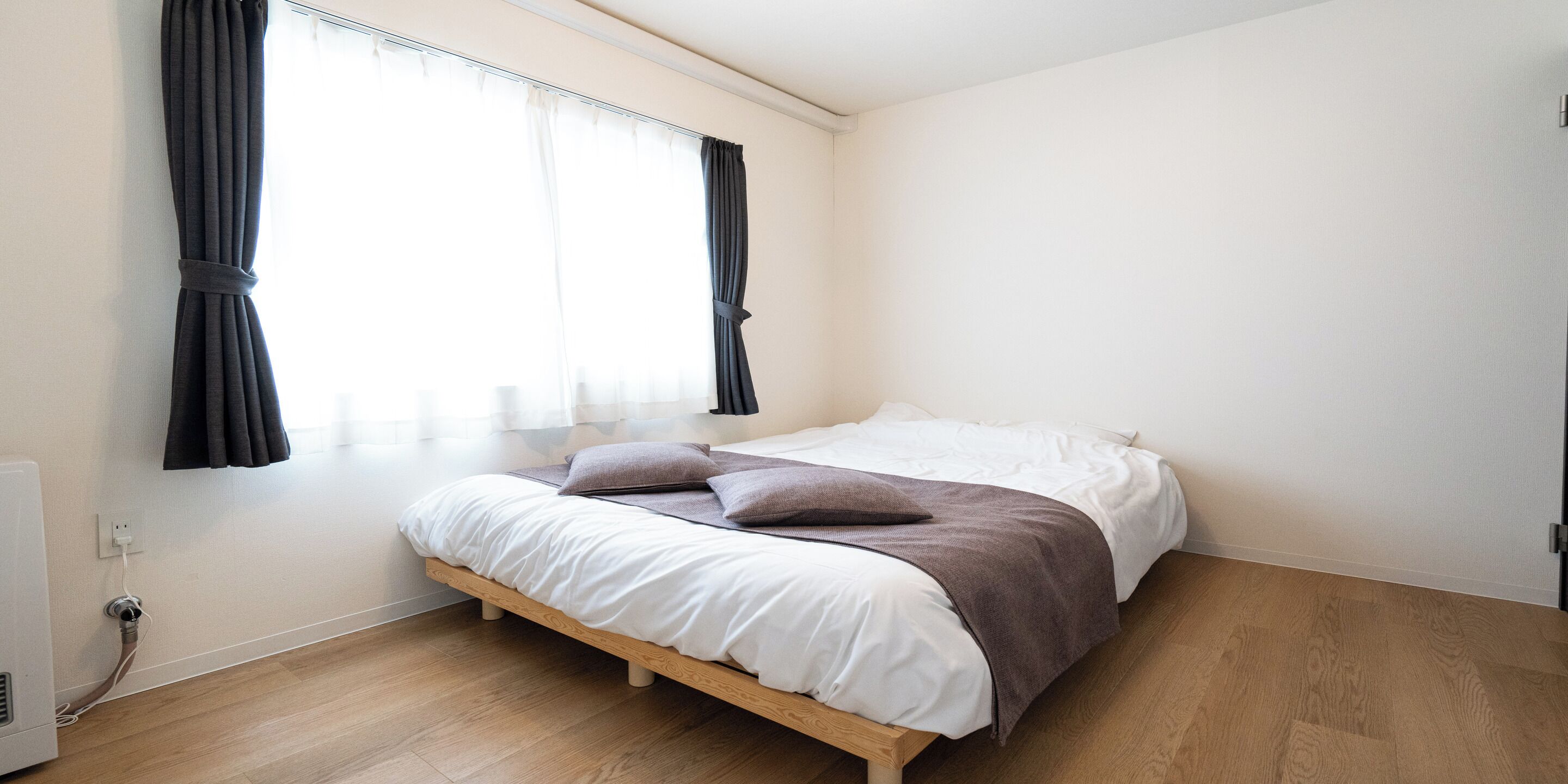 A bedroom with a bed, wooden floor, and a window with curtains.