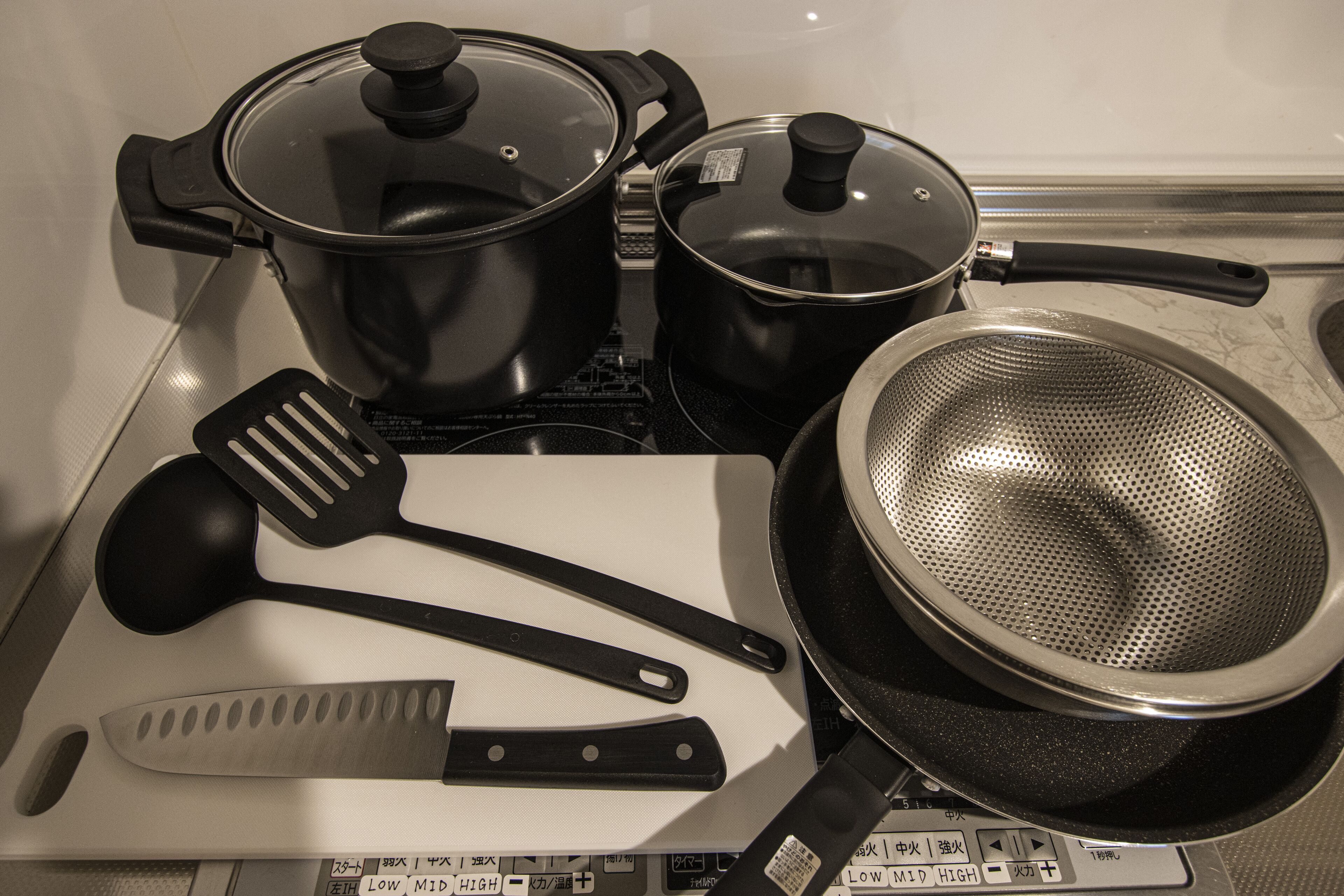 Une cuisine équipée d’une cuisinière, de casseroles, de poêles, d’une passoire, d’une spatule et d’un couteau.