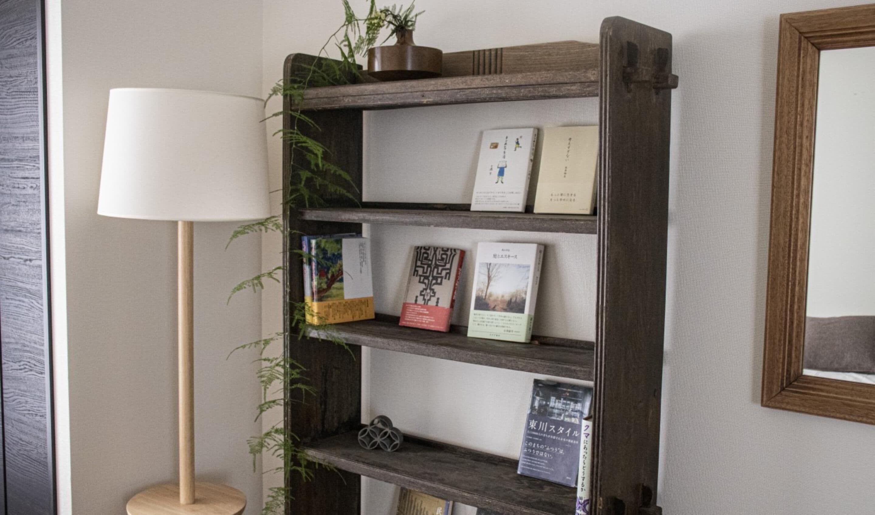 A bookshelf with books and decorative items, a floor lamp, and a small plant.