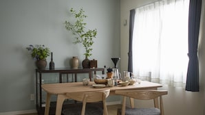 A dining area with a wooden table and chairs, a vase with flowers, and a coffee maker. - UCHI Susukino 5.7 (Sapporo)