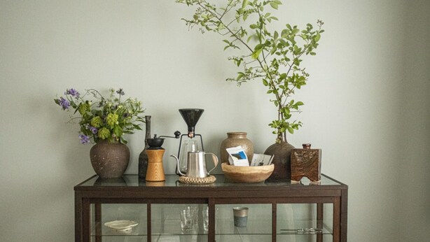 A wooden console table with various items including a vase with flowers, a coffee maker, a glass pitcher, and a small plant. - UCHI Susukino 5.7 (Sapporo)