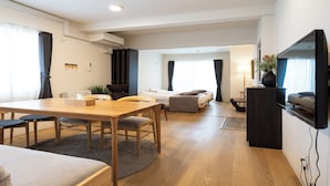 A modern hotel room with a wooden dining table, a sofa, a bed, and a TV mounted on the wall. - UCHI Susukino 5.7 (Sapporo)