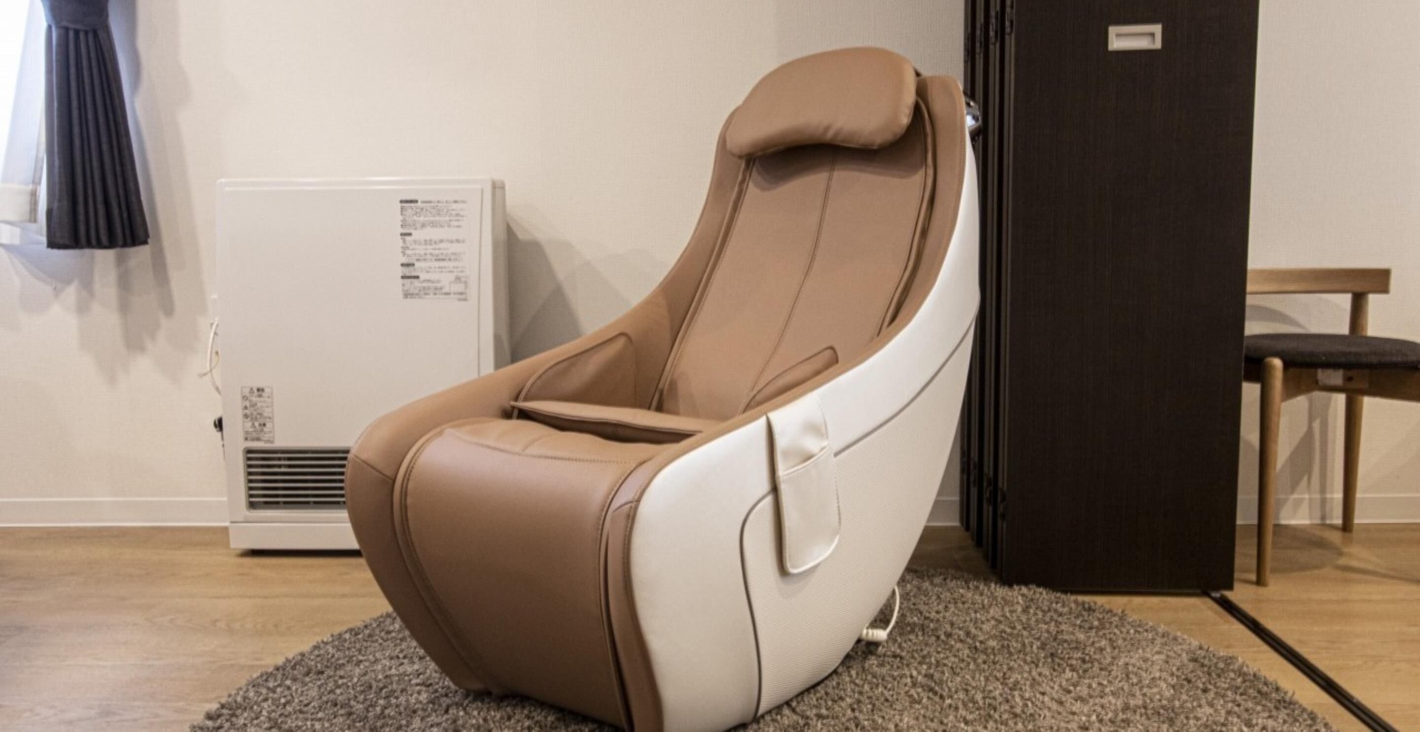 Ein Massagesessel in einem Raum mit Heizkörper, dunkler Tür und Holzstuhl.