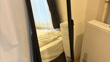 Una habitación con cama, un espejo de pie, una silla y un calefactor.