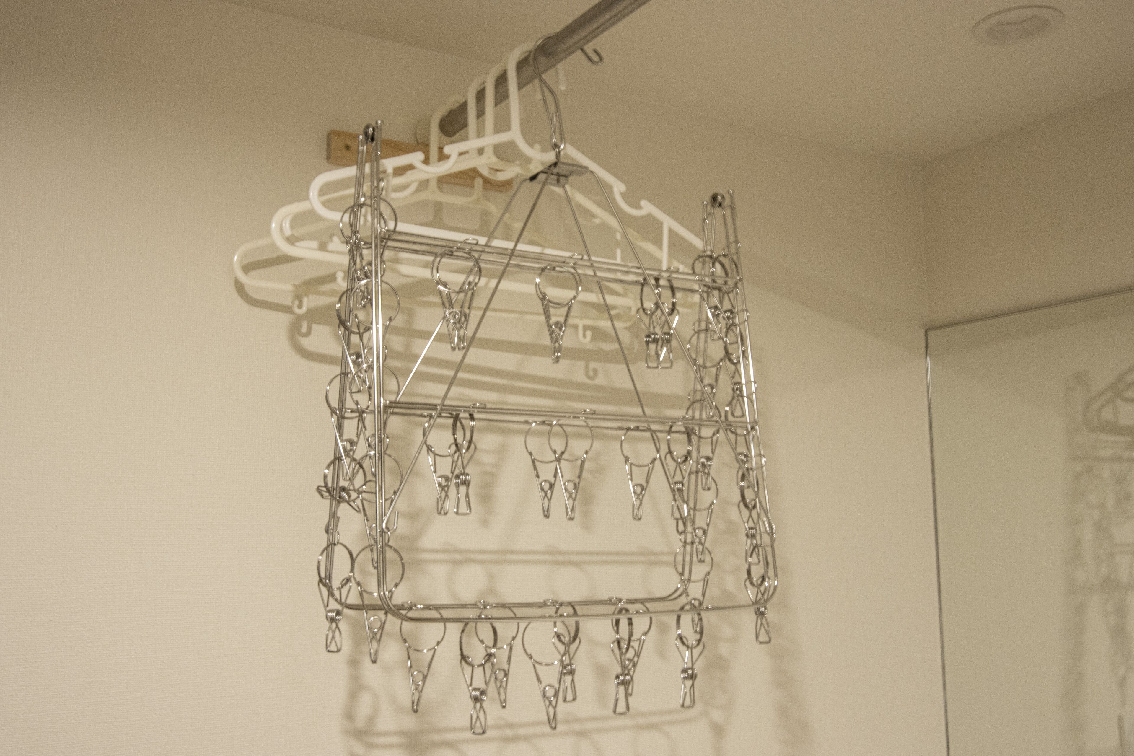 A metal drying rack with multiple hooks for hanging items, mounted on a wall.
