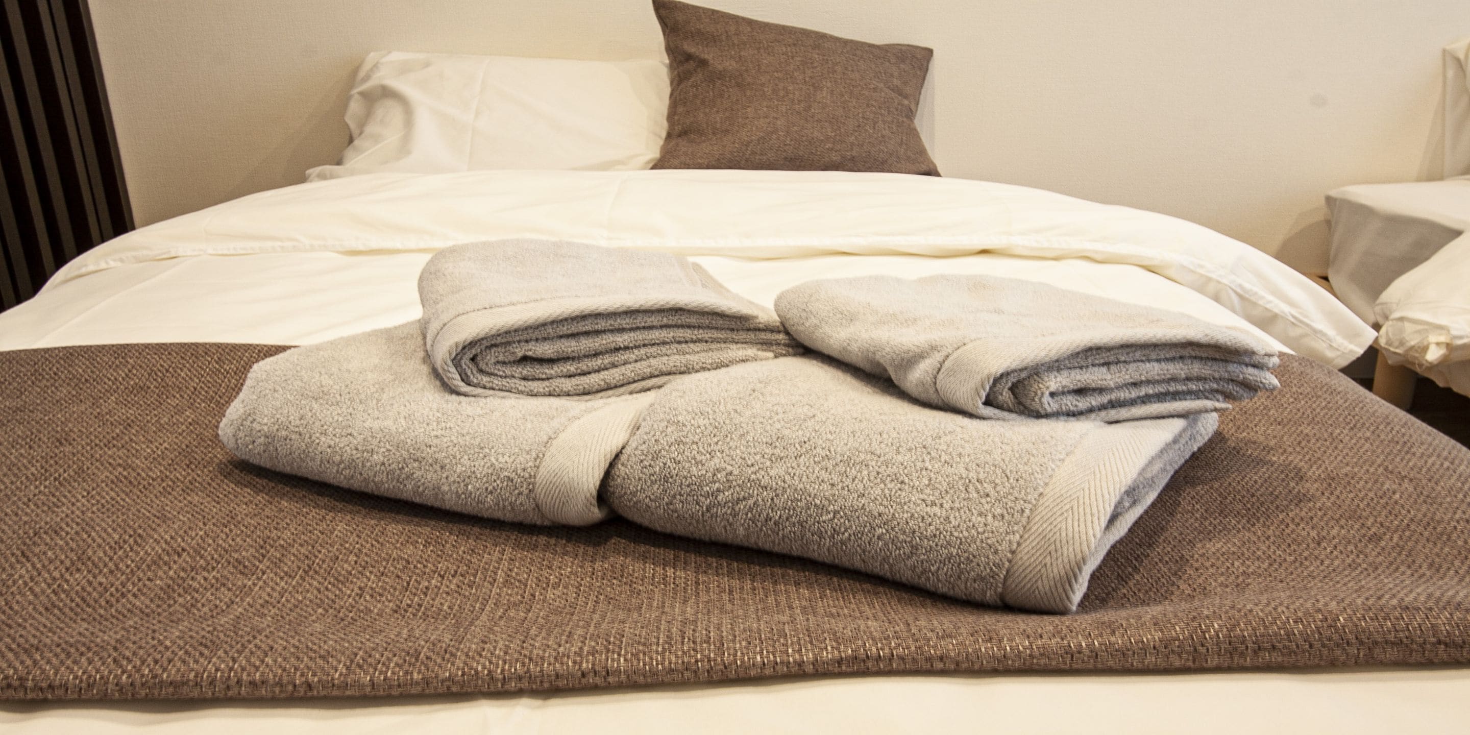 A neatly made bed with a folded towel and a brown blanket.