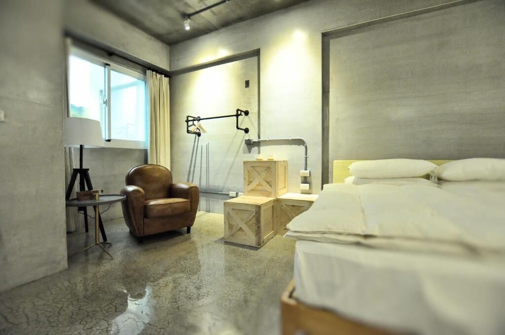 A hotel room with a bed, a chair, a desk, a lamp, and a window.
