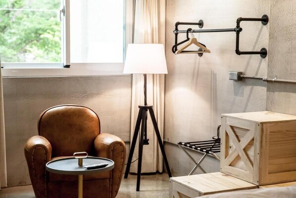 A room with a leather armchair, a small round table, a lamp, a wooden crate, and a wall-mounted drying rack. - Genuinn (Taitung)