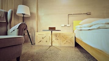 Una habitación de hotel con una cama, una silla, una mesita y una lámpara.