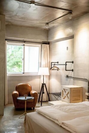 A hotel room with a bed, a chair, a small table, a lamp, a window, and a wardrobe. - Genuinn (Taitung)