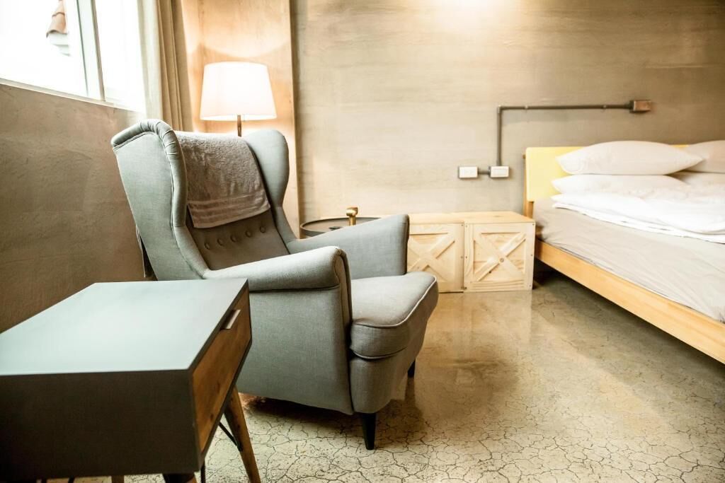 A hotel room with a bed, a chair, a small table, and a lamp.