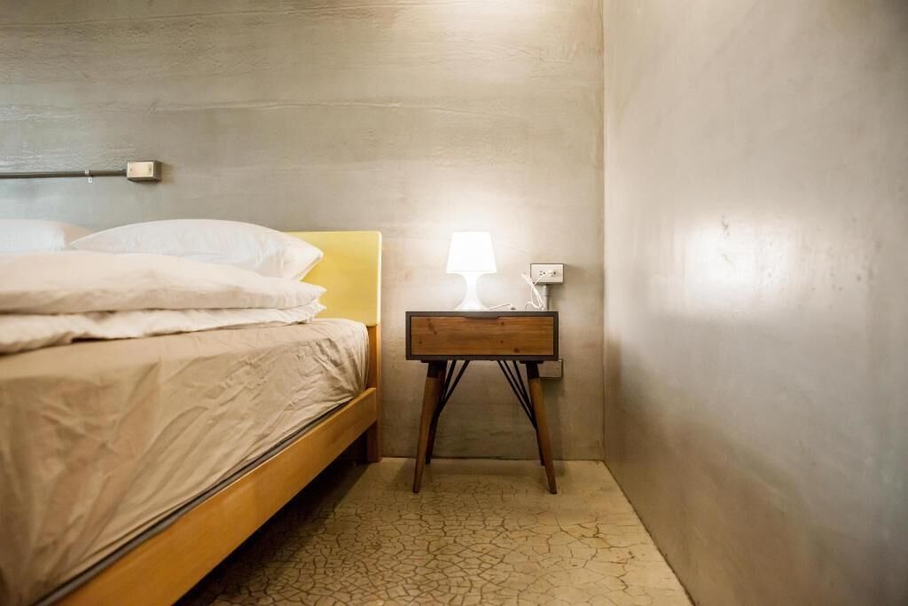 Un dormitorio con una cama, una mesita de noche con lámpara y una lámpara de pared.
