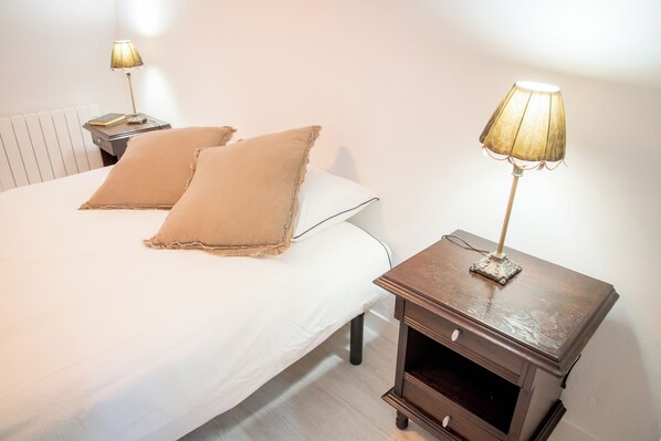 A neatly made bed with two pillows, a bedside table with a lamp, and a radiator in the background.