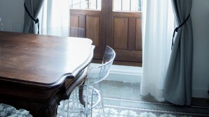 A room with a wooden table, a clear chair, and a view through a door with curtains.