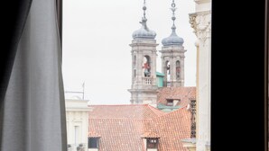 A view from a window with a balcony, featuring a building with a bell tower and red-tiled roofs.