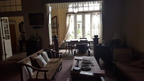 A traditional living room with a sofa, dining table, and chairs. There is a window with curtains, a fireplace, and a wall-mounted fish decoration.